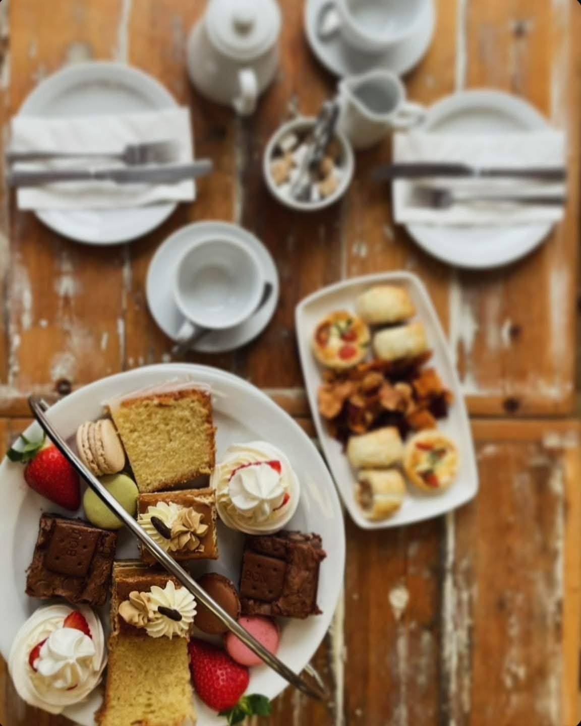 Flat-lay of an afternoon tea spread with cakes, macarons and table settings