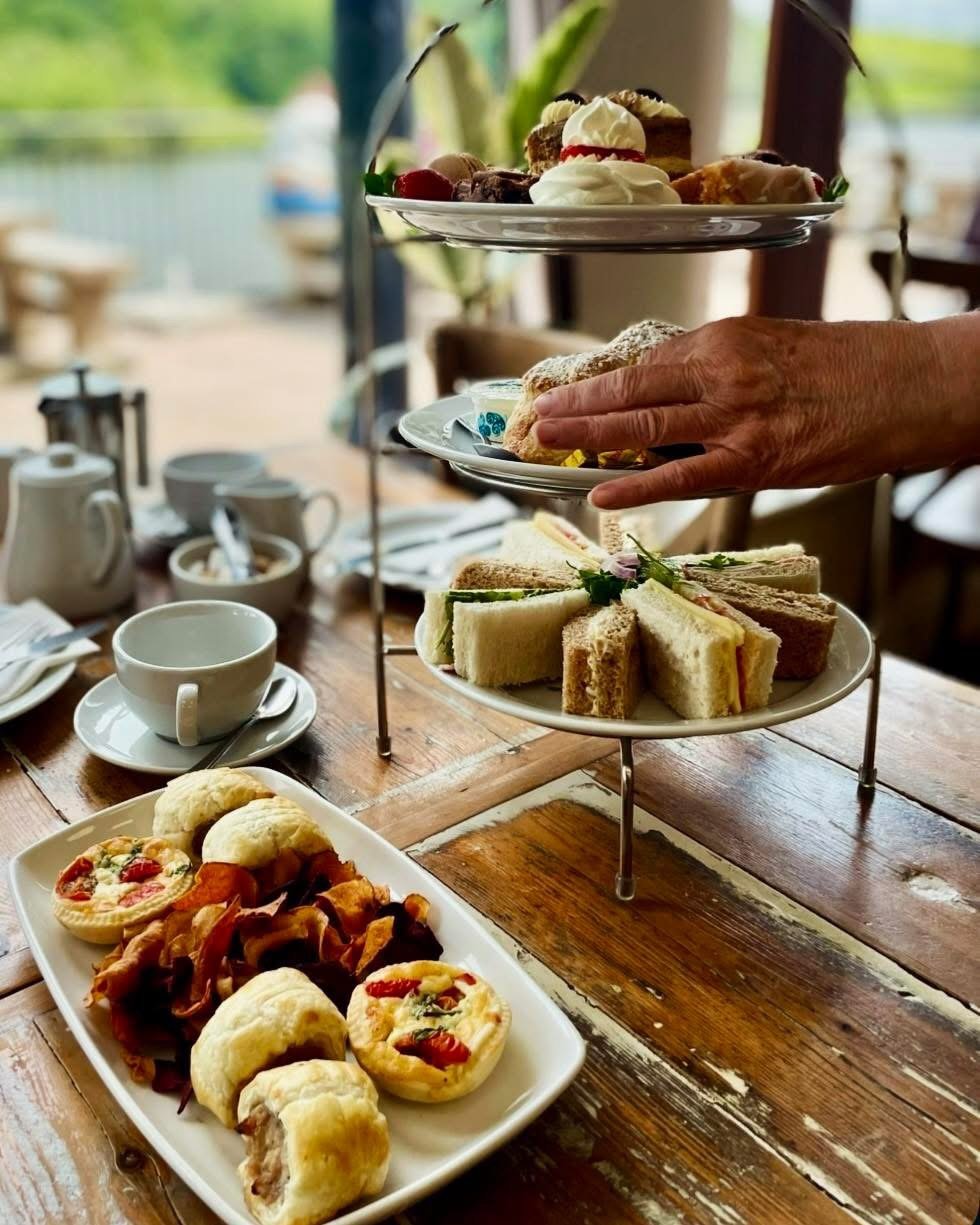 Tiered afternoon tea stand with scones, cakes and sandwiches, lake view behind