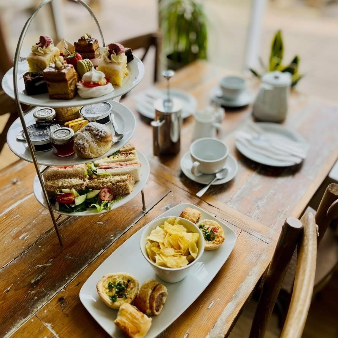 Full afternoon tea spread with a tiered stand and side platter of quiches and sausage rolls