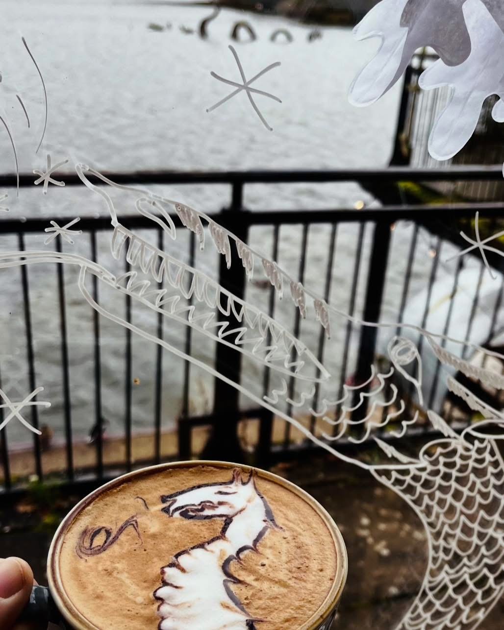 A latte with etched glass art and the lake visible behind