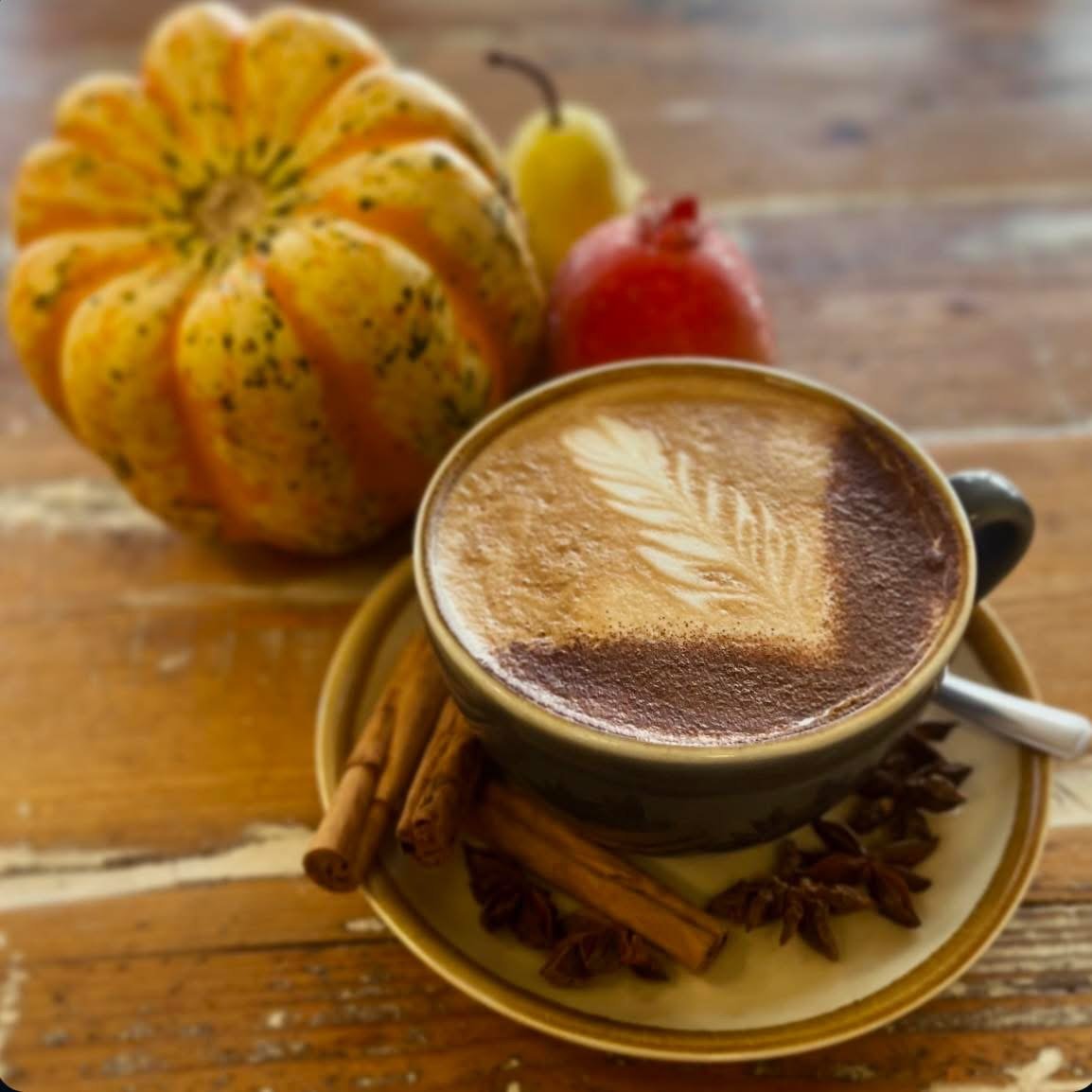 A spiced latte with leaf-pattern art and cinnamon sticks