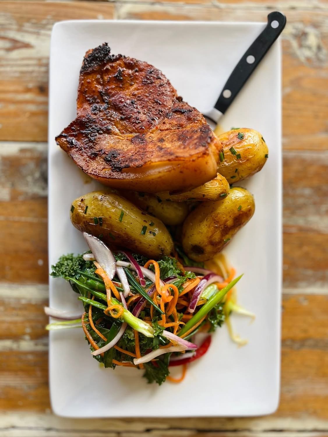 A grilled pork chop with potatoes and kale slaw